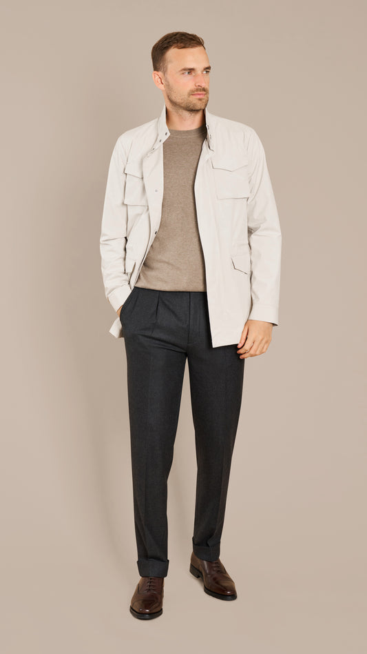 Man wearing a Ivory Lightweight Field Jacket, brown shirt, dark pants, and brown shoes on a beige background