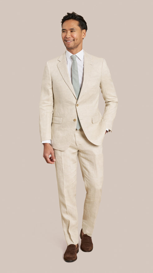 Man wearing a beige suit with a white shirt and brown shoes on a plain background