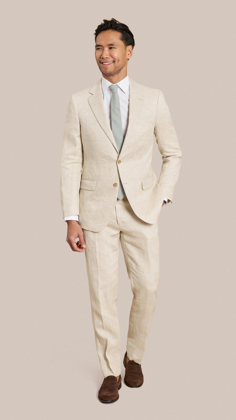Man wearing a beige suit with a white shirt and brown shoes on a plain background