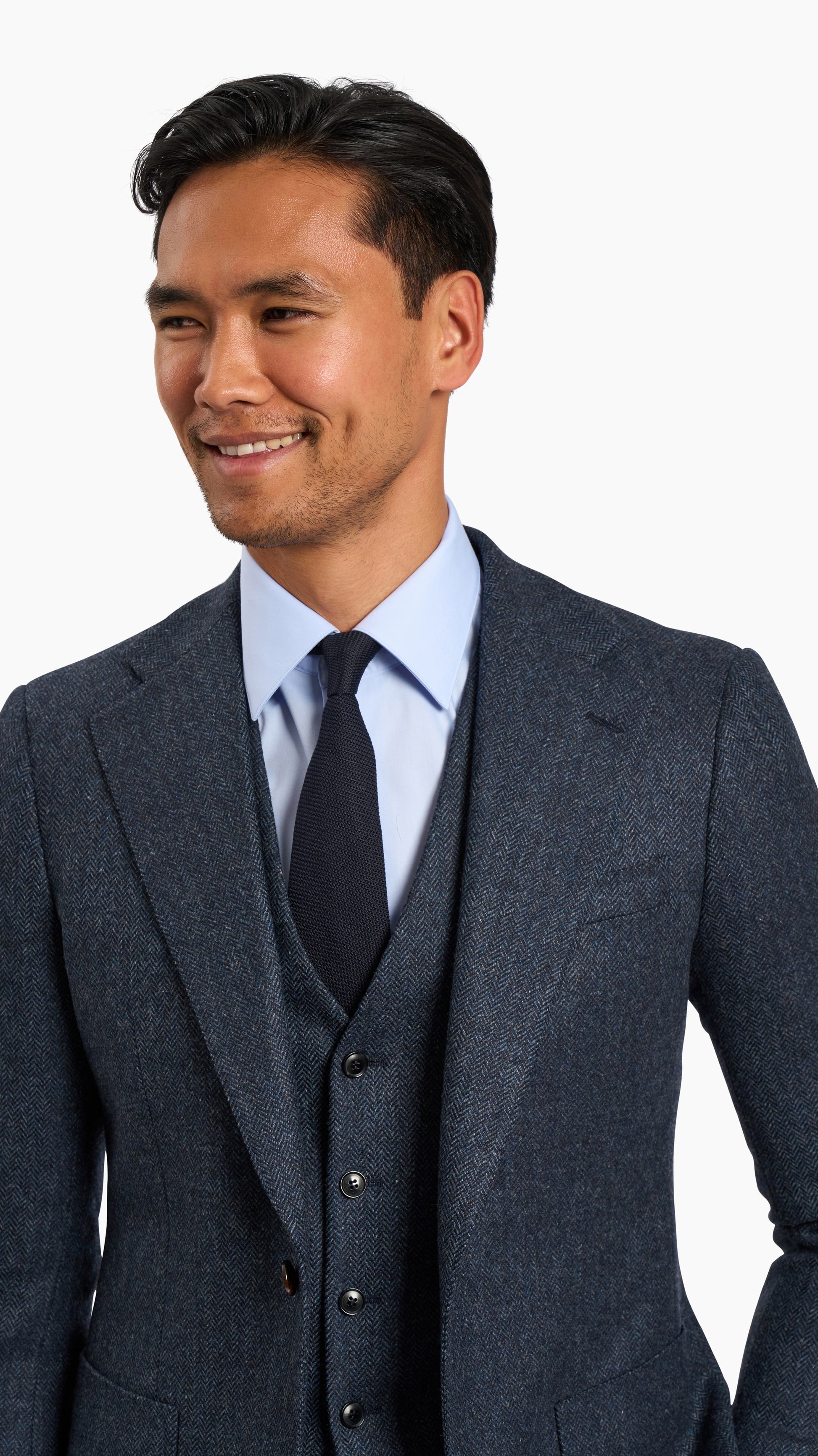 Man wearing Abraham Moon Navy Tweed Suit with textured wool fabric, light blue shirt, and navy tie smiling.